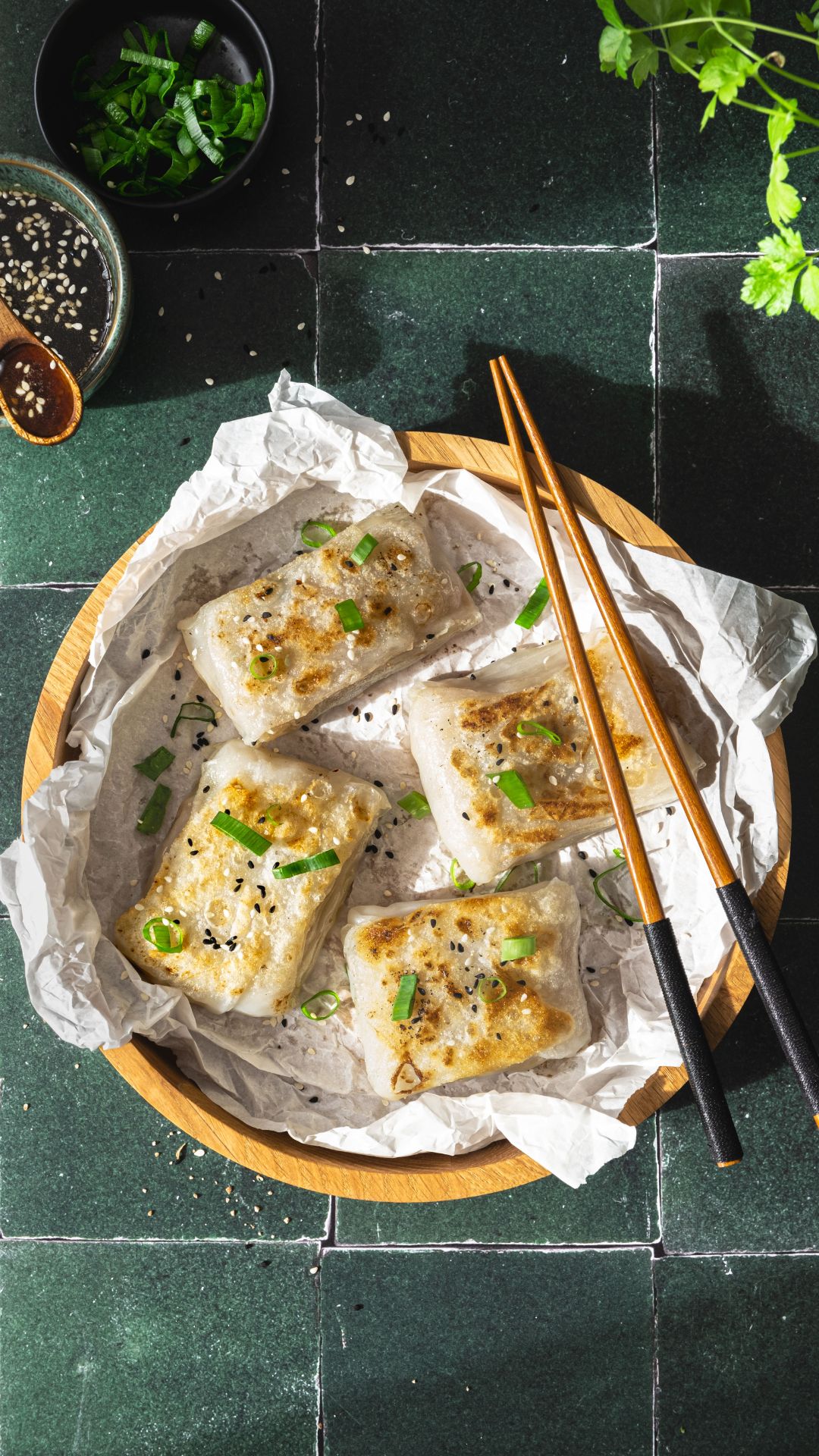 Knusprige Reispapier Dumplings in einer Holzschale. Ein Schälchen mit Honig-Sauce und einem Holzlöffel. Essstäbchen aus Holz. Petersilie-Blätter und ein Schälchen mit Frühlingszwiebel-Ringe.